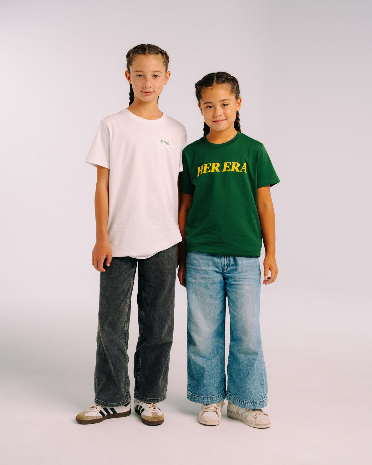 Her Era Statement Youth tee in Core Green, worn in studio, full length alongside a white KS Label youth tee – KS Label