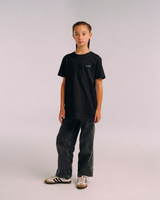 Model wearing the front of the black SHE CAN Youth tee by KS Label