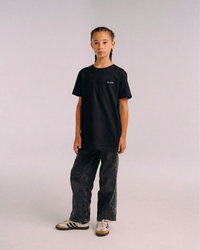 Model wearing the front of the black SHE CAN Youth tee by KS Label