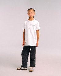 Model wearing the front of the white SHE CAN Youth tee by KS Label
